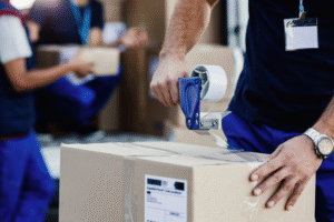 Close-up-of-worker-using-tape-dispenser-while-packing-cardboard-box-for-a-delivery